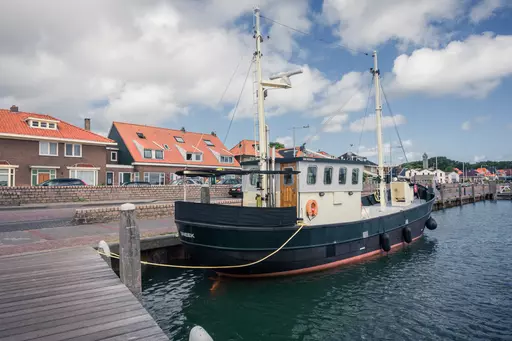 Schiff im Hafen von Terschelling: Ein traditionelles Schiff liegt am Steg, umgeben von bunten Häusern und Wasser.