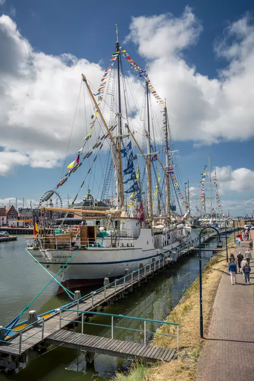 Sailing ship in Harlingen: A festively decorated ship rests by a calm canal as pedestrians stroll along the walkway.