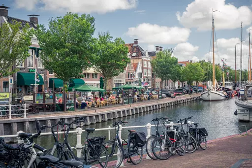 Bicycles line the canal's edge, surrounded by storefronts and bustling terraces filled with patrons.