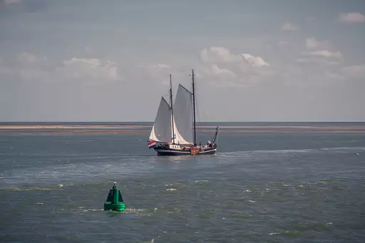 Sailing boat off Vlieland: A traditional sailboat with large white sails glides across a calm water surface.