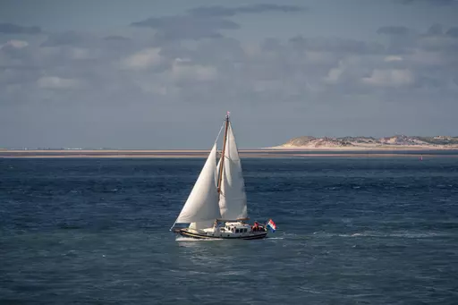 Sailing boat off Vlieland: A white boat with large sails glides over deep blue water, with sand dunes and beaches in the background.