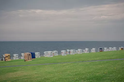 Colorful beach chairs are lined up on a green lawn near the water under a slightly overcast sky.