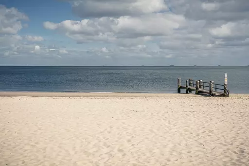 Strand auf Föhr: Ein ruhiger Sandstrand mit Wasser im Hintergrund und einem kleinen Holzsteg auf der rechten Seite.