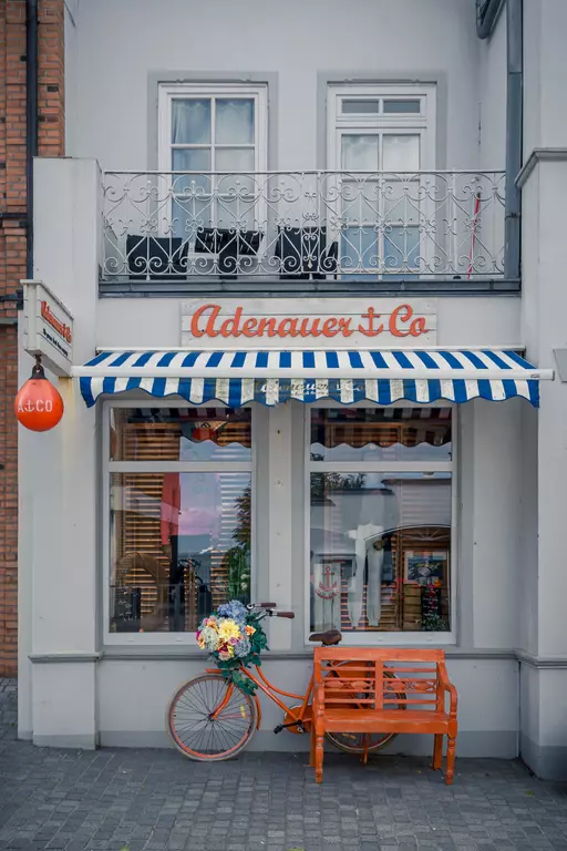 Föhr: Schickes Geschäft mit blau-weiß gestreifter Markise, orangefarbenem Fahrrad und Holzbank vor der Tür.