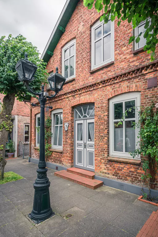 Backsteinarchitektur in Föhr: Eine charmante, rote Backstein-Fassade mit einem Eingang, umgeben von grünen Pflanzen und einer Laterne.