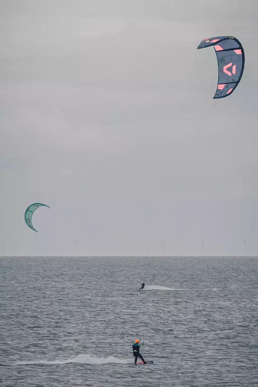 Kitesurfen auf Sylt: Ein Kitesurfer fährt über das Wasser, während zwei Kites über ihm in der Luft schweben.