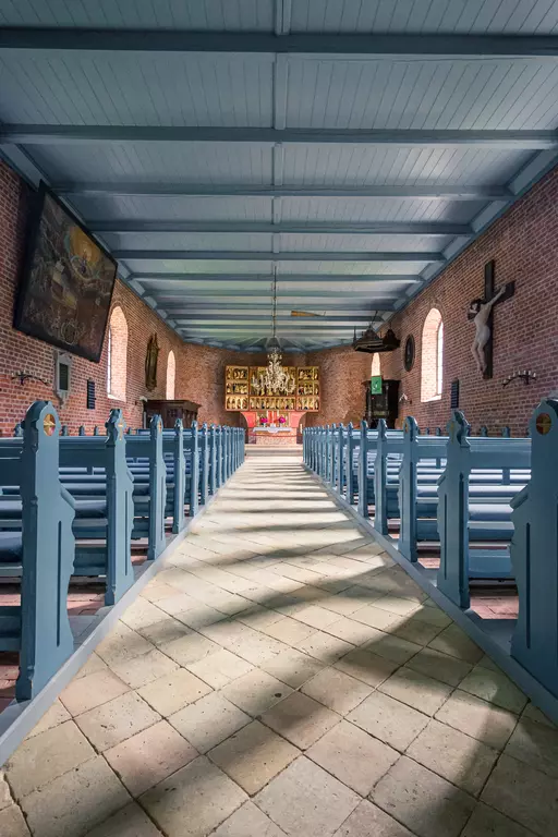 Blick auf den Innenraum einer Kirche mit hellblauen Bänken, Holzböden und sanftem Licht von Fenstern.