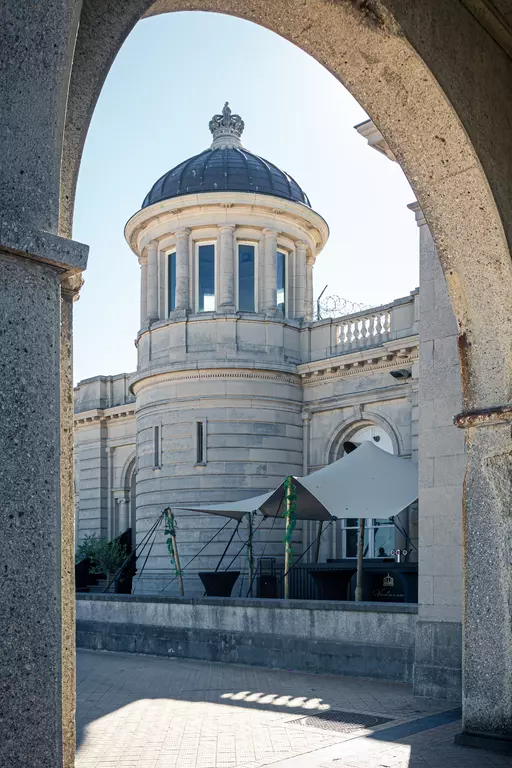 A view through an archway of a historic building featuring a dome and an outdoor area with visible plants.