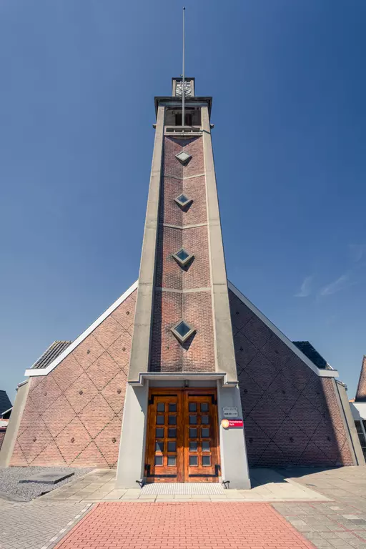 A modern hexagonal church with a trapezoidal facade and large wooden doors, set against a blue sky.