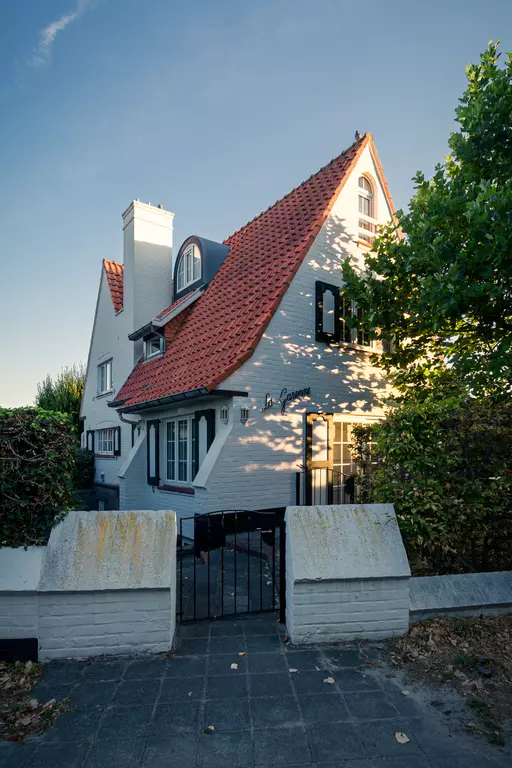 Ein helles, zweigeschossiges Haus mit rotem Satteldach, weißen Wänden und einem geschlossenen Gartenzaun.