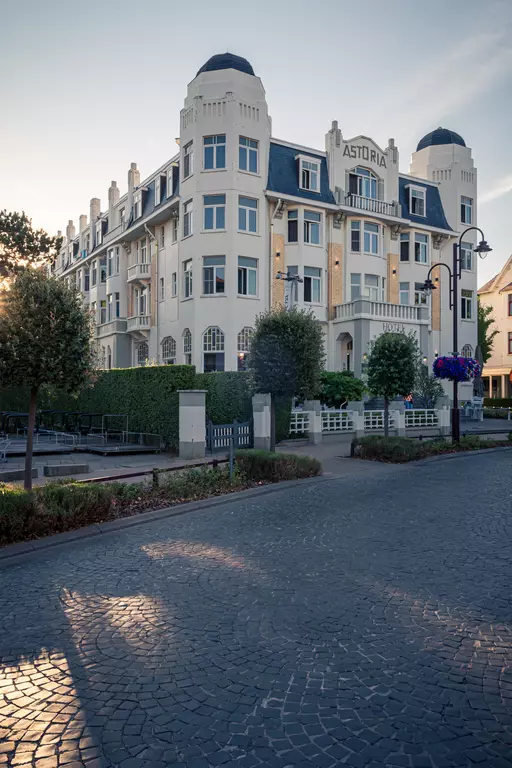 Ein elegantes, historisches Gebäude mit hellem Anstrich und Erkern. Umgeben von Bäumen und Blumenkästen.