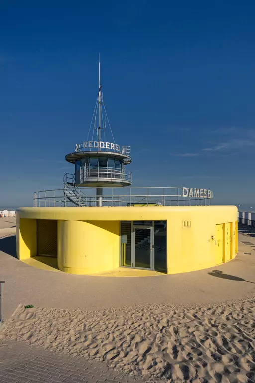 A round, yellow lifeguard tower with an upper deck, surrounded by fine sand and a clear blue sky.