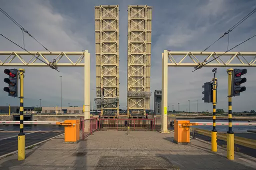 Hochgezogene Klappbrücke zwischen zwei Türmen, mit blinkenden Signalen und Schranken, die den Zugang zur Straße kontrollieren.