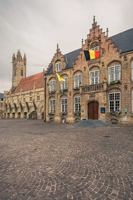 A historic brick building with colorful flags and a tower in the background, surrounded by cobblestones.