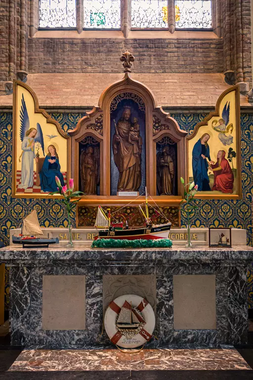 A wooden altar featuring a statue and images of religious figures, flanked by a model ship and a stone plaque.