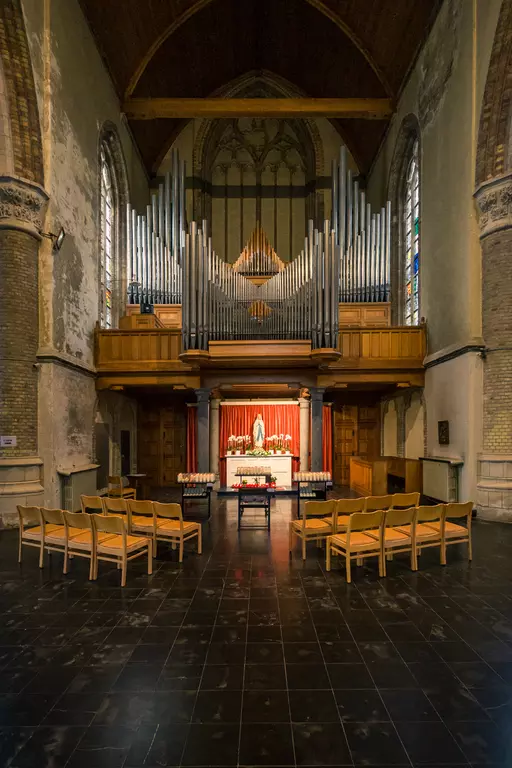 An interior view of a church featuring wooden pews, an altar, a statue, and a large pipe organ in the background.