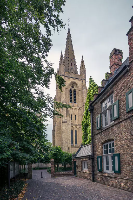 A narrow path leads to a tall, pointed church, surrounded by trees and old brick-paved houses.