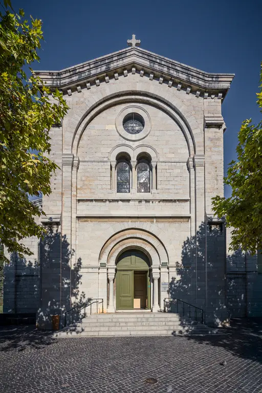 Eingang der Église Saint-Michel de Cassis, mit steinerner Fassade und grünen Türen. Umgeben von Bäumen und gepflastertem Boden.