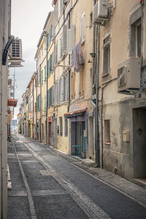 A narrow street in La Ciotat featuring tall, weathered buildings, colorful shutters, and a quiet atmosphere.