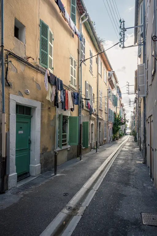 A narrow street in La Ciotat lined with colorful buildings and laundry hanging between them, creating a quaint, charming atmosphere.
