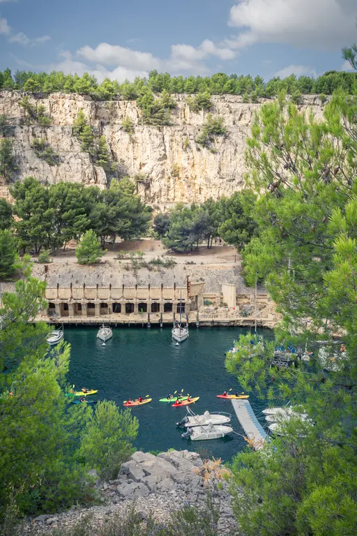 Blick auf den Calanque von Port-Miou in Cassis, mit steilen Felsen, grünen Bäumen und Kajakfahrern auf dem klaren Wasser.