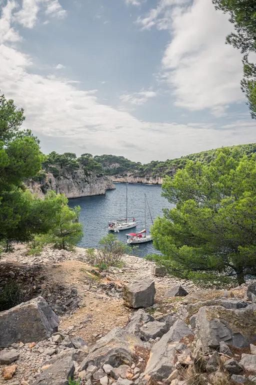 Blick auf die Calanque von Port-Miou in Cassis. Zwei Segelboote liegen ruhig im Wasser, umgeben von felsigen Klippen und dichten Bäumen.