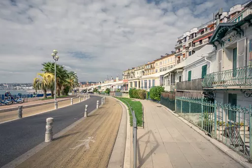 View of a winding promenade with palm trees and historic buildings lining the coast under a cloudy sky.