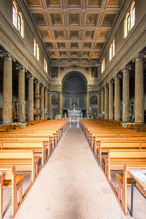 Bright church hall with tall columns, wooden pews in rows, and intricate ceiling design. The altar is clearly visible at the end of the aisle.