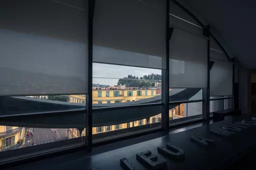 View from a window with blinds, showing a cityscape and hills in the background.