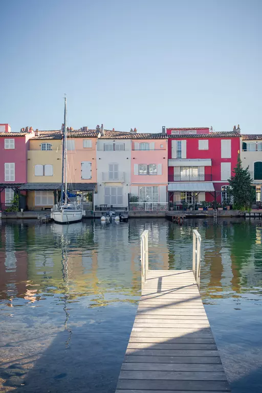 Eine Holzplattform führt zu einem Kanal, umgeben von bunten Häusern in Pastelltönen und einem Boot im Wasser.