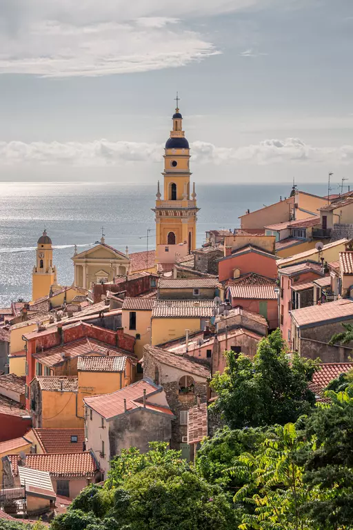 Colorful houses in Menton: A view of the townscape featuring the church tower and the shimmering sea in the background.