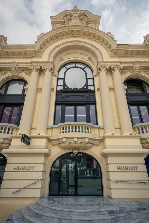 An opulent building with large windows and intricate architectural details, featuring an entrance marked by Hublot signage.