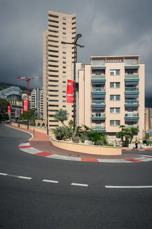 High-rise buildings and modern residences surround a winding road, with green plants and a construction crane in the background.