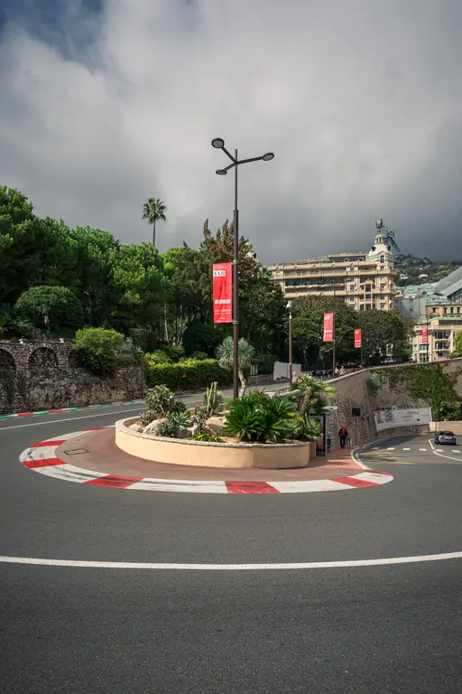 A winding road with a large roundabout, surrounded by green trees and buildings in Monaco.