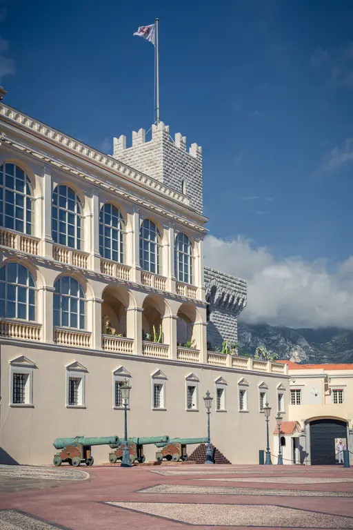 View of a historic building with tall windows and a tower, alongside old cannons on a square.