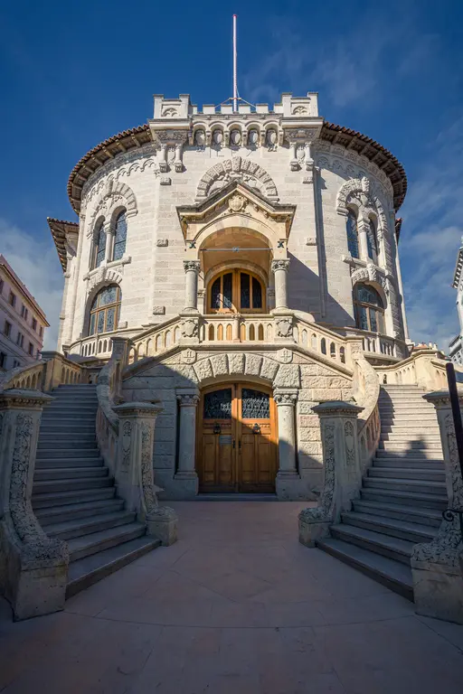 An impressive round stone facade with ornate details and large windows, surrounded by a winding staircase.