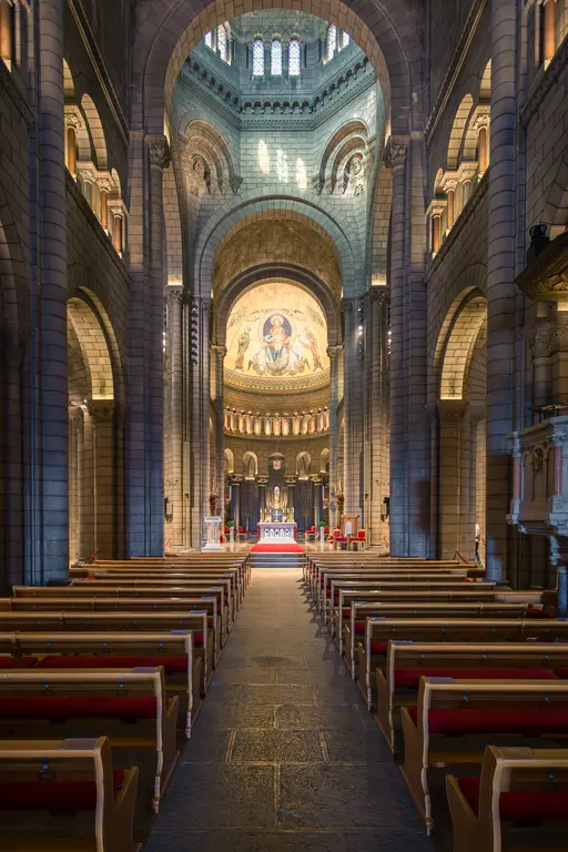 A large, bright church featuring high vaulted ceilings and rows of wooden benches. An altar and a golden dome are visible in the background.