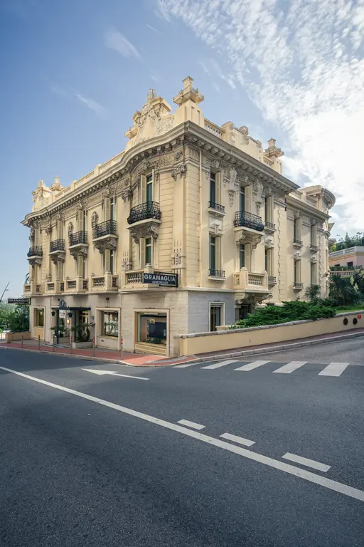 An elegant, historic building with a yellow façade, balconies, and a shop on the ground floor along a busy street.