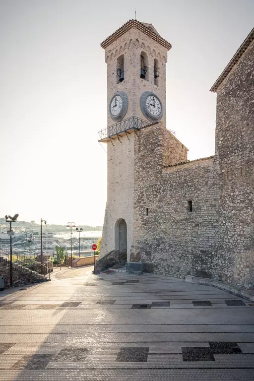 Eglise Notre-Dame d’Espérance in Cannes: Eine Steinkirche mit Uhrturm und gepflasterter Straße im Vordergrund.