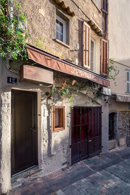 Eine schmale Gasse mit einem Gebäude, das eine braune Markise trägt. Das Restaurant-Schild „Le Marichou“ und eine dunkle Holzfronttür sind sichtbar.