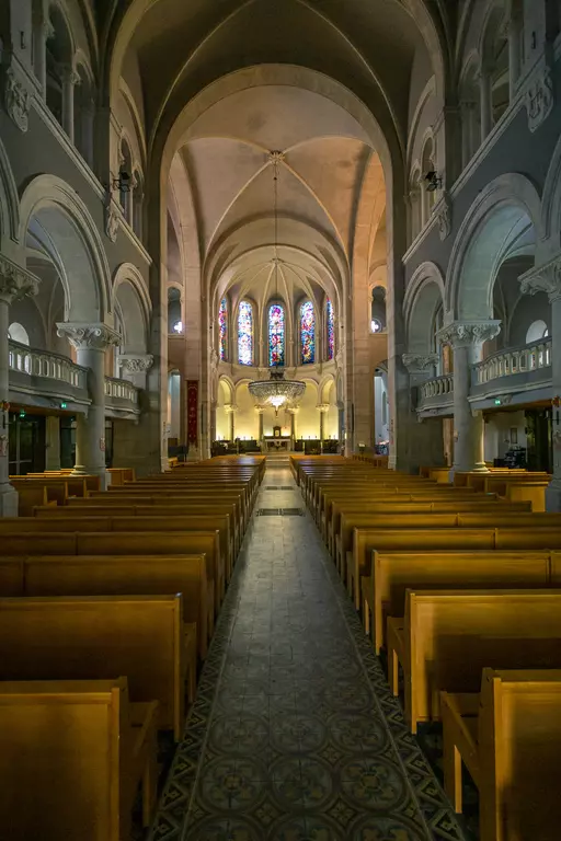 Ein langer Kirchensaal mit Holzbankreihen, hohen Decken und bunten Fensterkuppeln, die sanftes Licht auf den Boden werfen.