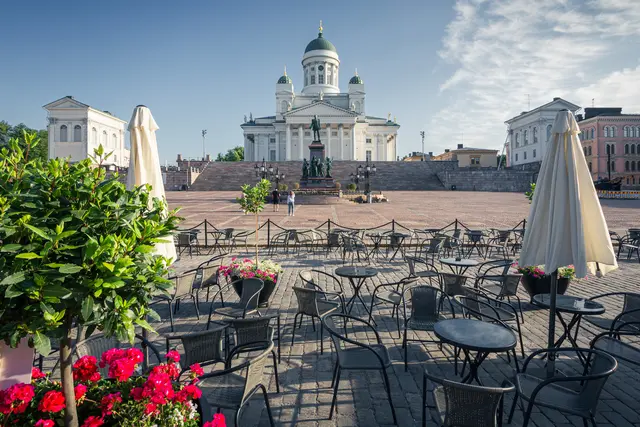 A vibrant outdoor café with empty tables and blooming flowers in front of a grand white cathedral.