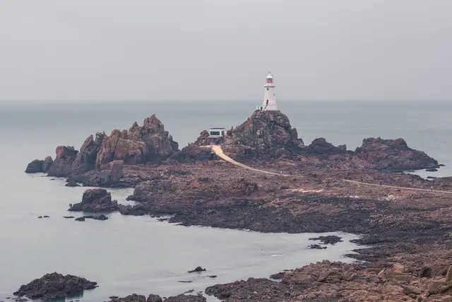 Leuchtturm auf felsiger Insel, umgeben von ruhigem Wasser. Die Strukturen sind in grauer Umgebung leicht sichtbar.