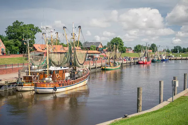 Blick auf den idyllischen Hafen von Greetsiel mit traditionellen Fischkuttern und ruhigem Wasser.