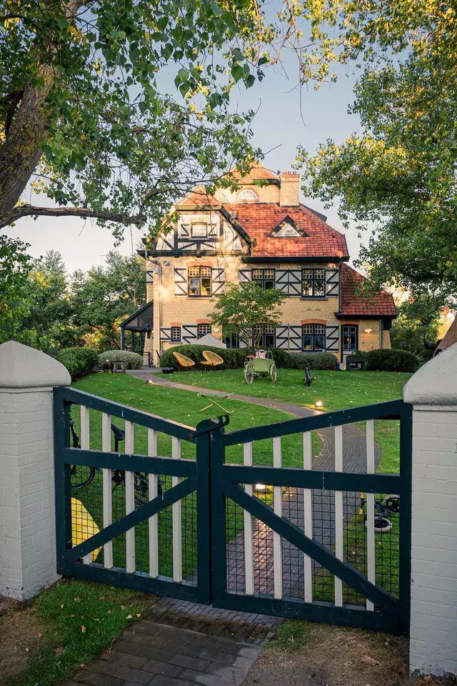 A green garden gate opens to a charming two-story house with a red gabled roof and elegant half-timbered details.