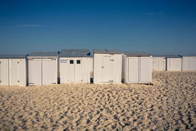 White beach huts line up against bright sand under a clear blue sky.