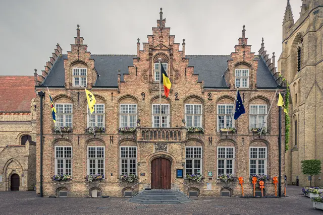 Rathaus von Nieuwpoort: historisches Backsteingebäude mit vielen Fenstern, flaggen dekoriert, umgeben von gepflanzten Blumen.