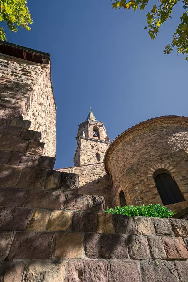 A stone staircase leads up to a historic church with a tall, pointed tower under a clear blue sky.