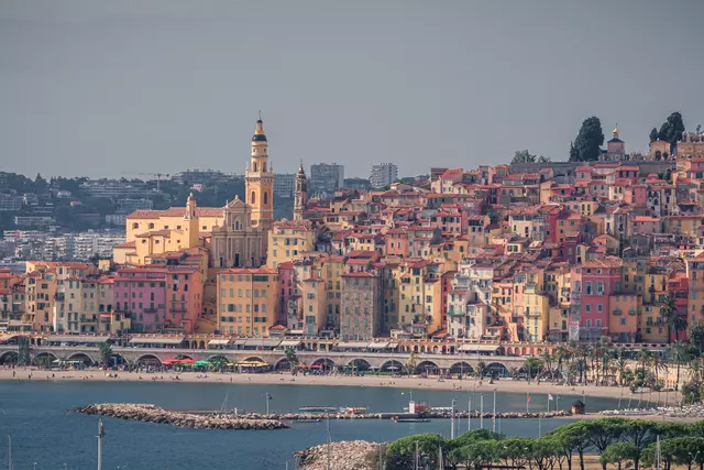 Bunte Stadtansicht von Menton, mit historischen Gebäuden und einer Strandpromenade am Wasser.