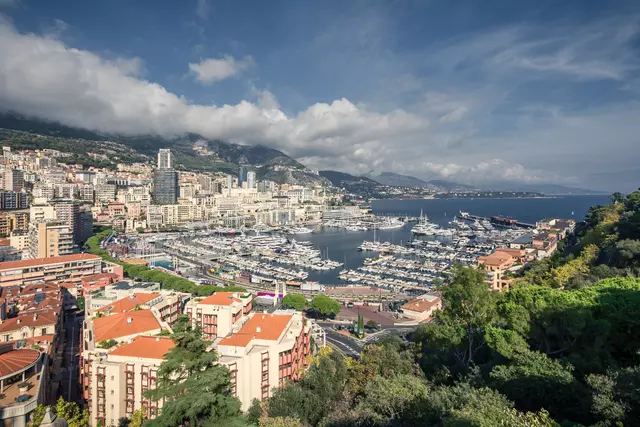 harbor of Monaco: view of the harbor with yachts, surrounded by city buildings and hills under a partly cloudy sky.